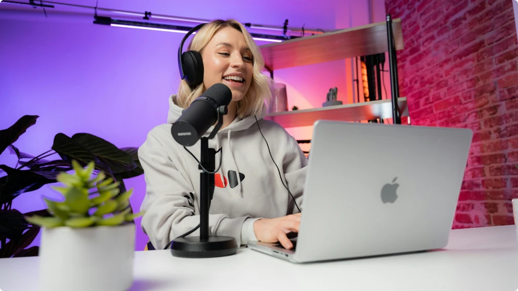 Blond woman smiling and recording a podcast with a microphone, macbook and audio interface in a recording studio - Audio Interface for Podcasting