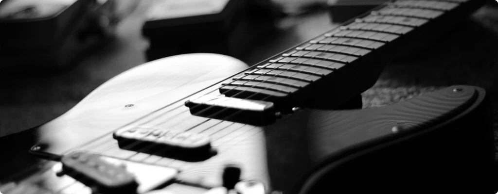 Black and white close up of an electric guitar with some pedals and the best audio interface for guitar in the background