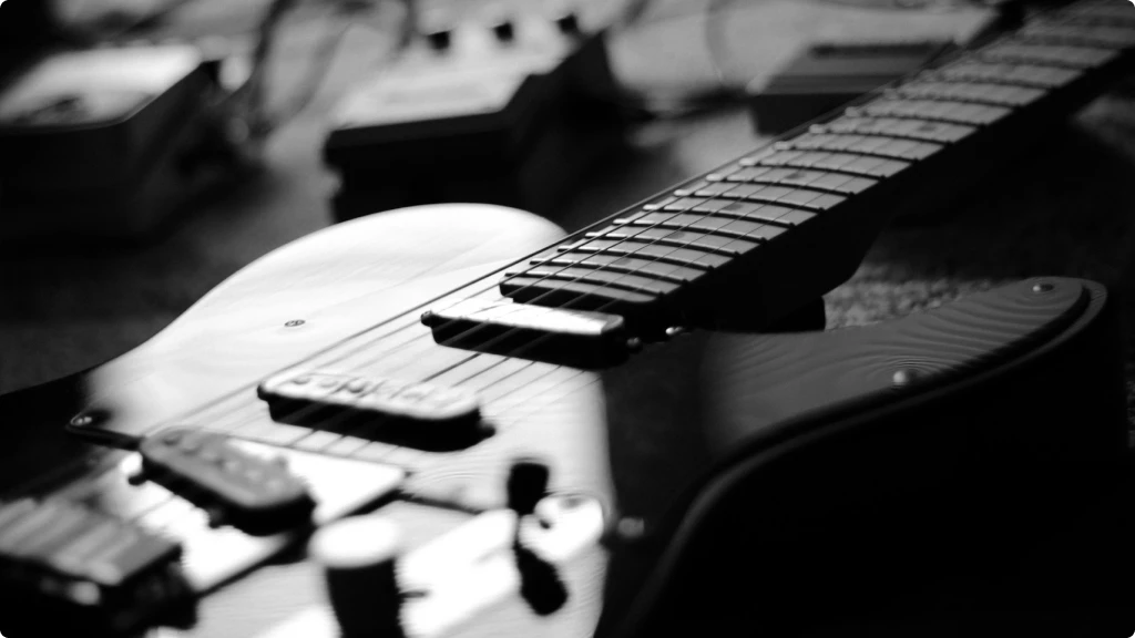 Black and white close up of an electric guitar with some pedals and the best audio interface for guitar in the background