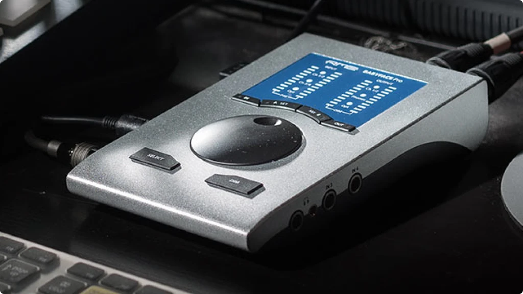 A RME Babyface Pro FS audio interface resting on a desk, indicating a workspace for audio recording tasks.